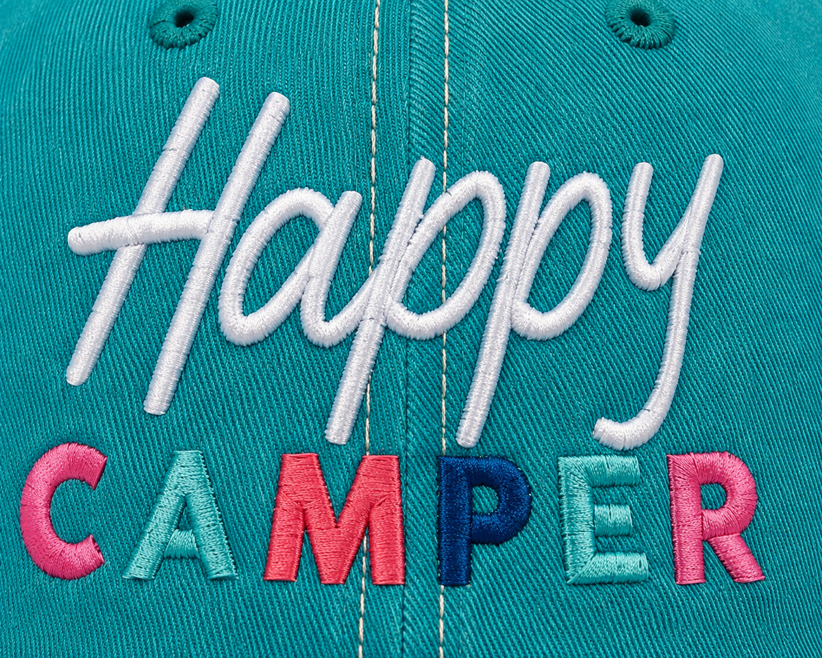 Close-up of multicolor embroidered "Happy Camper" lettering on a distressed teal trucker hat front panel.

