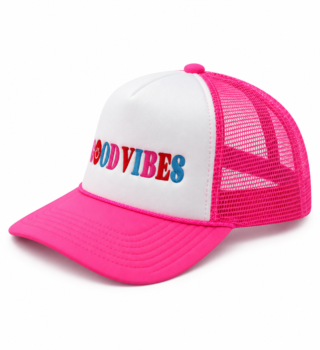 Good Vibes Trucker Hat three-quarter angle view showing white structured front, hot pink bill and mesh back, and multicolor embroidered Good Vibes lettering with smiley face detail on white background
