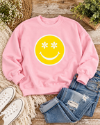 Light pink Daisy Eyes sweatshirt styled with distressed jeans, white sneakers, flowers, and greenery on rustic wood
