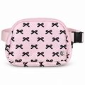 Pink Bow Belt Bag and Crossbody front view showing pink nylon with all-over black bow print, top zipper main compartment, silver Katydid K logo rivet, and adjustable pink satin strap with black side-release buckle on white background
