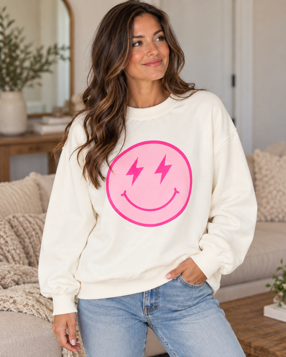 Model wearing the cream sweatshirt with a pink smiley face and hot pink lightning-bolt eyes, paired with jeans
