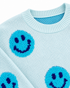 Close-up of the light blue sweater showing its ribbed crew neckline and textured turquoise happy faces with dark blue eyes and smiles
