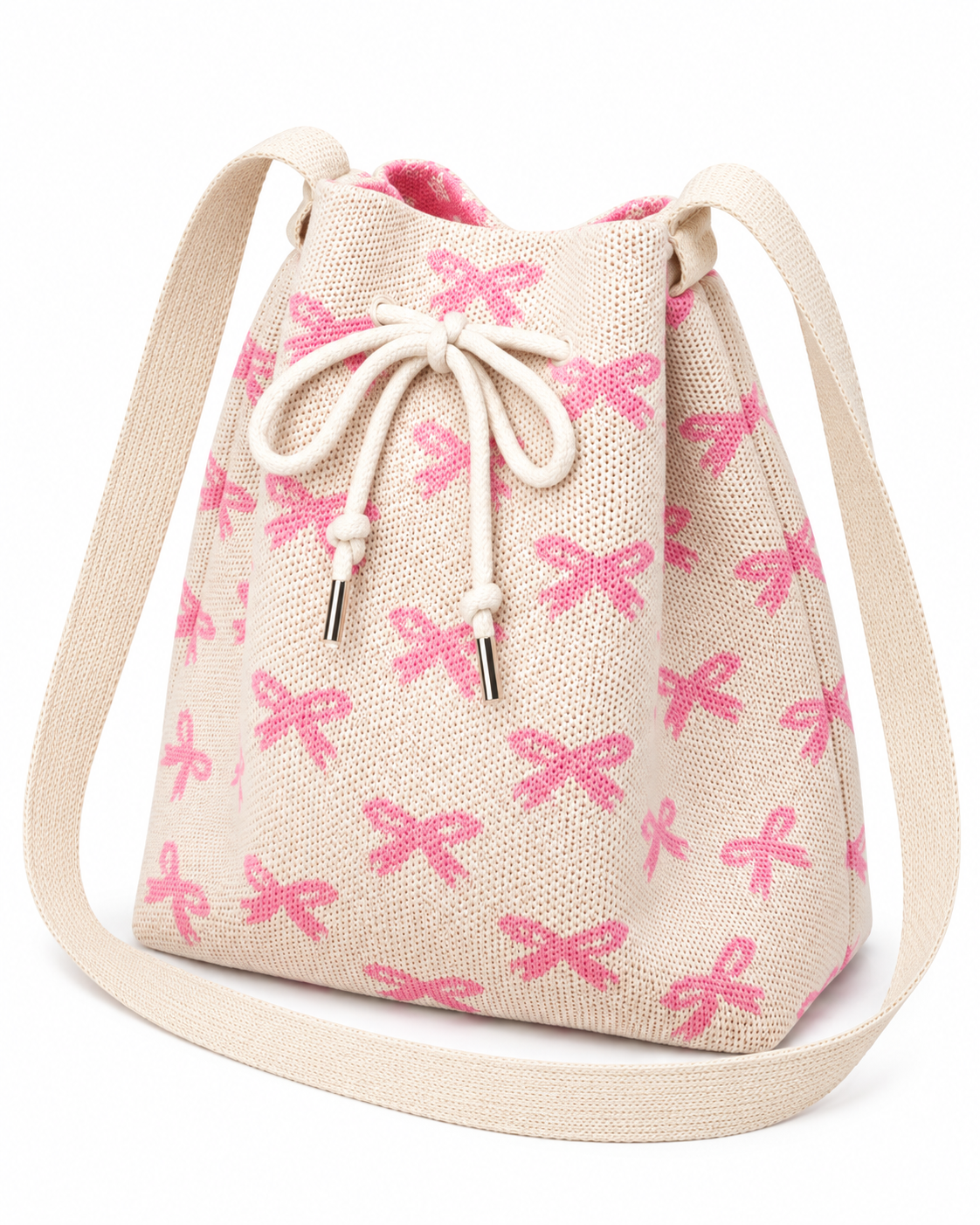 Coquette Bow Crossbody Bucket Bag three-quarter angle view showing cream woven knit fabric with allover pink bow pattern, tapered bucket silhouette wider at top, cream rope drawstring closure with silver aglet tips, and wide flat cream crossbody strap on white background
