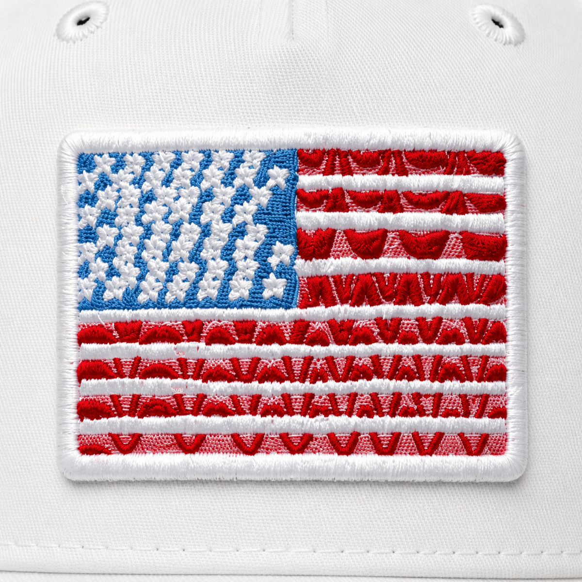 Close-up of embroidered American flag patch in red, white, and blue on a white baseball cap front panel with navy brim.

