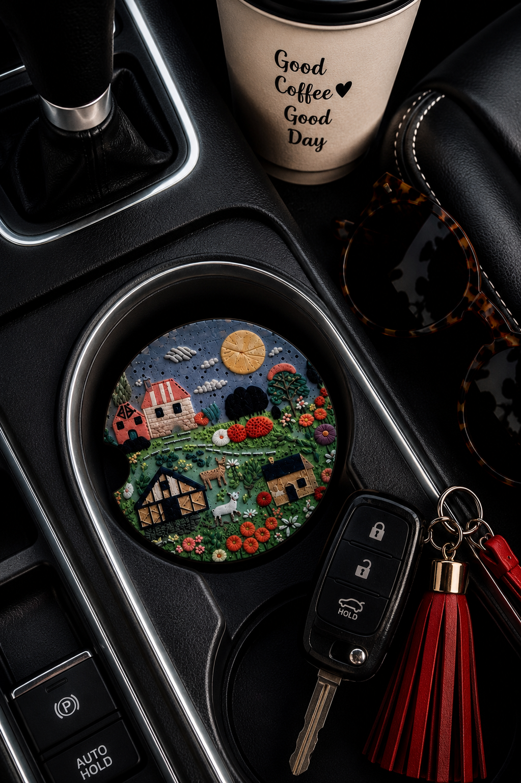 Folk Art Farm Village ceramic car coaster in cup holder — sculpted folk art farmhouses, goats, wildflowers, and yellow sun design, shown in car console with coffee cup and sunglasses

