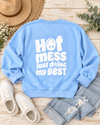Back of the light blue Hot Mess sweatshirt styled flat with jeans, cream sneakers, a tan hat, flowers, and greenery
