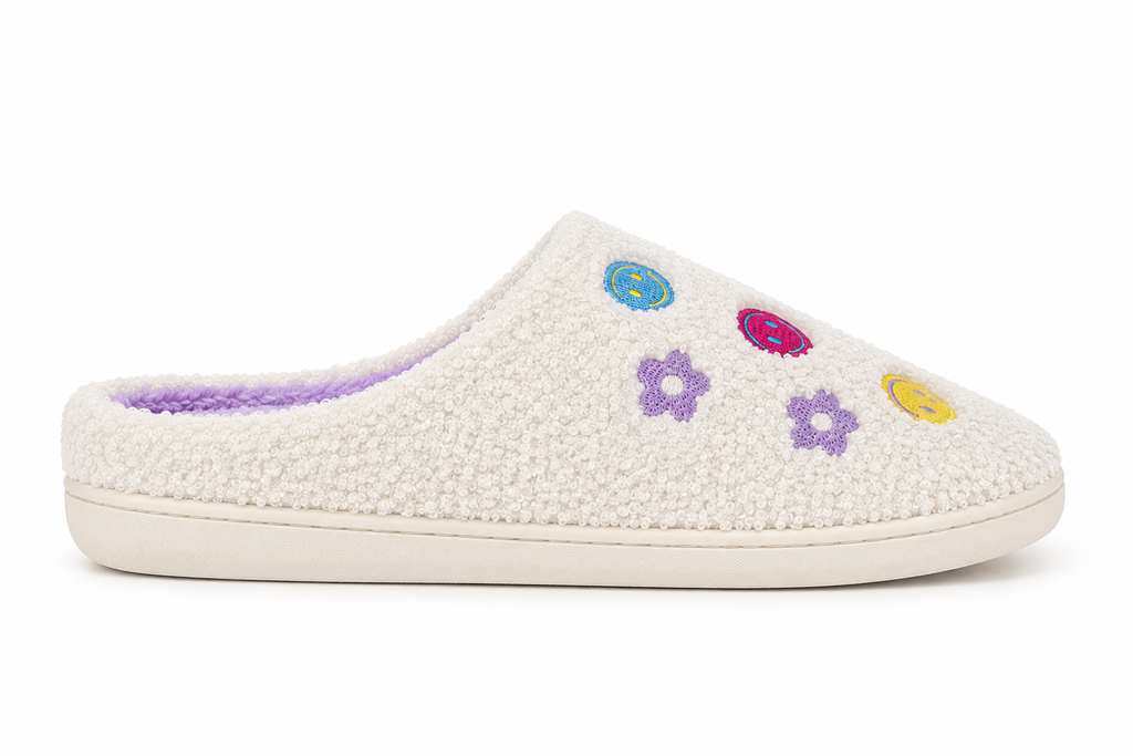 Side profile of one Ivory Smiley Face Fuzzy Slipper showing ivory fuzzy exterior with colorful embroidered smiley faces and purple daisy flowers, lavender interior lining, and cream rubber sole

