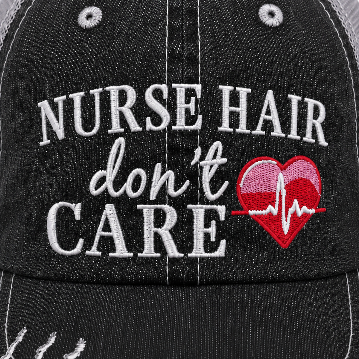 Close-up of a black trucker-style cap with white embroidered text reading 'NURSE HAIR don't CARE' and a red heart with a white heartbeat line.