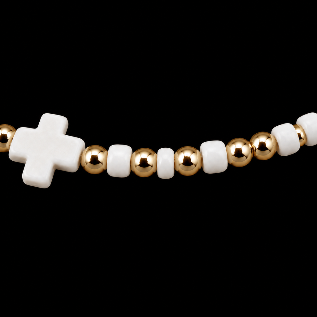 Close-up of white cross centerpiece flanked by white seed beads and polished gold-tone round beads on stretch bracelet
