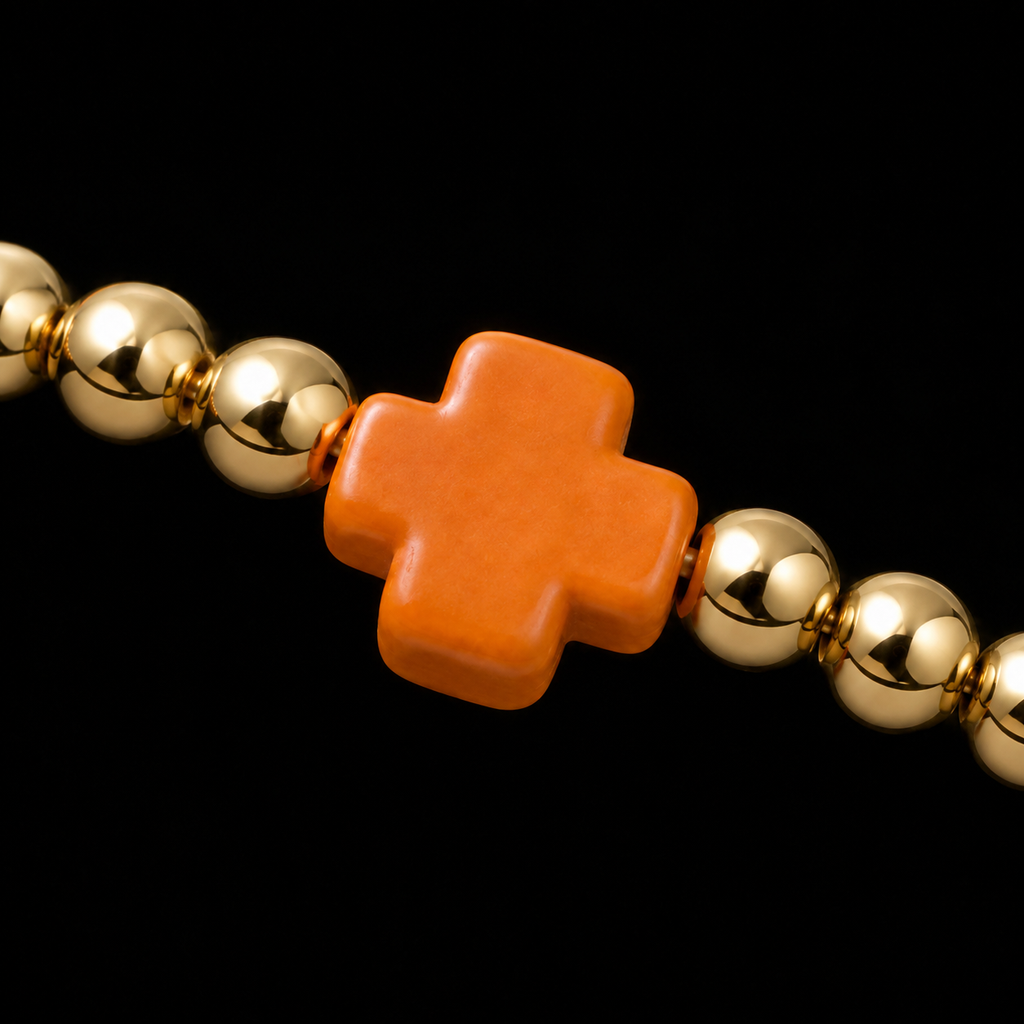 Close-up of polished gold-tone ball bead and bold orange cross accent bead on stretch bracelet
