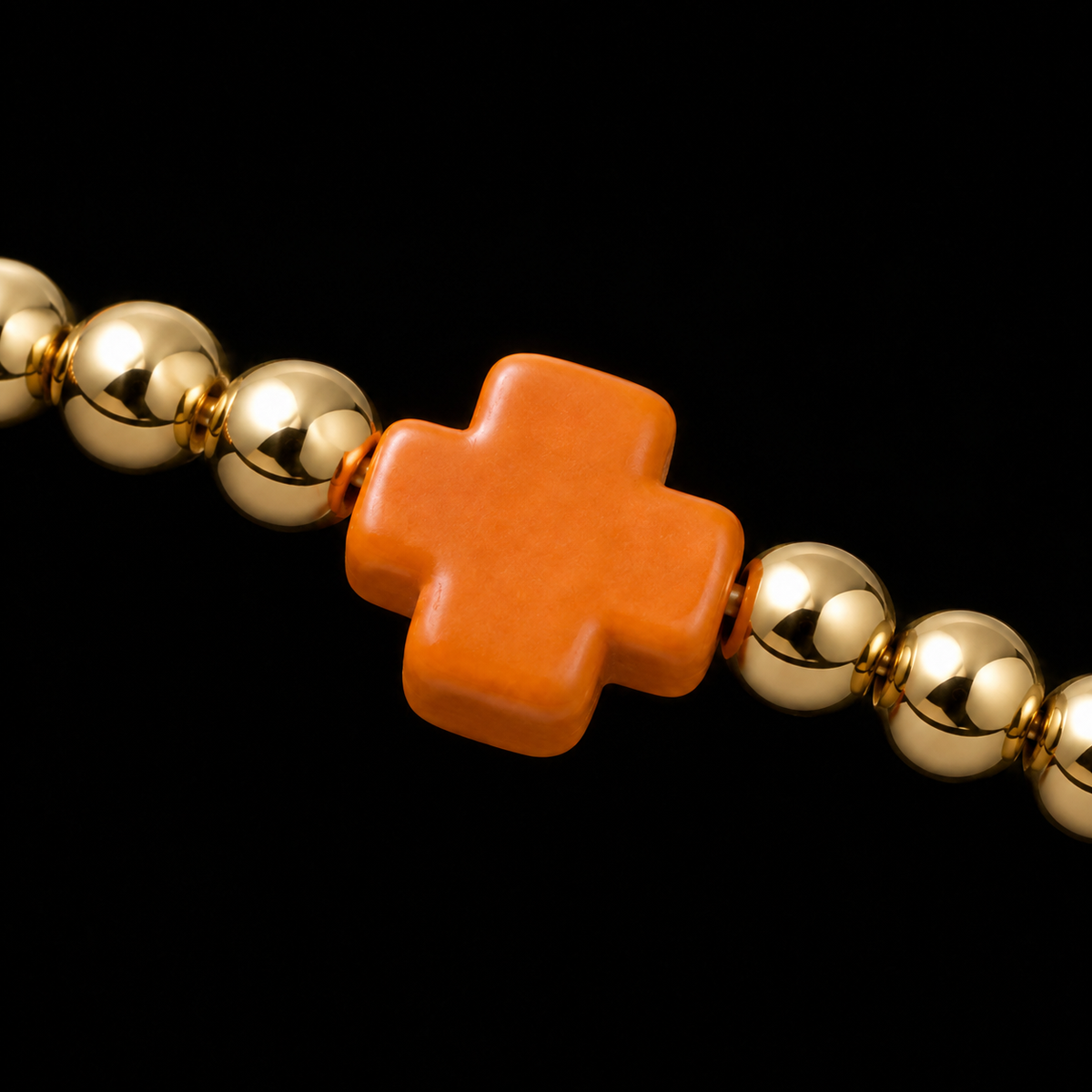Close-up of polished gold-tone ball bead and bold orange cross accent bead on stretch bracelet
