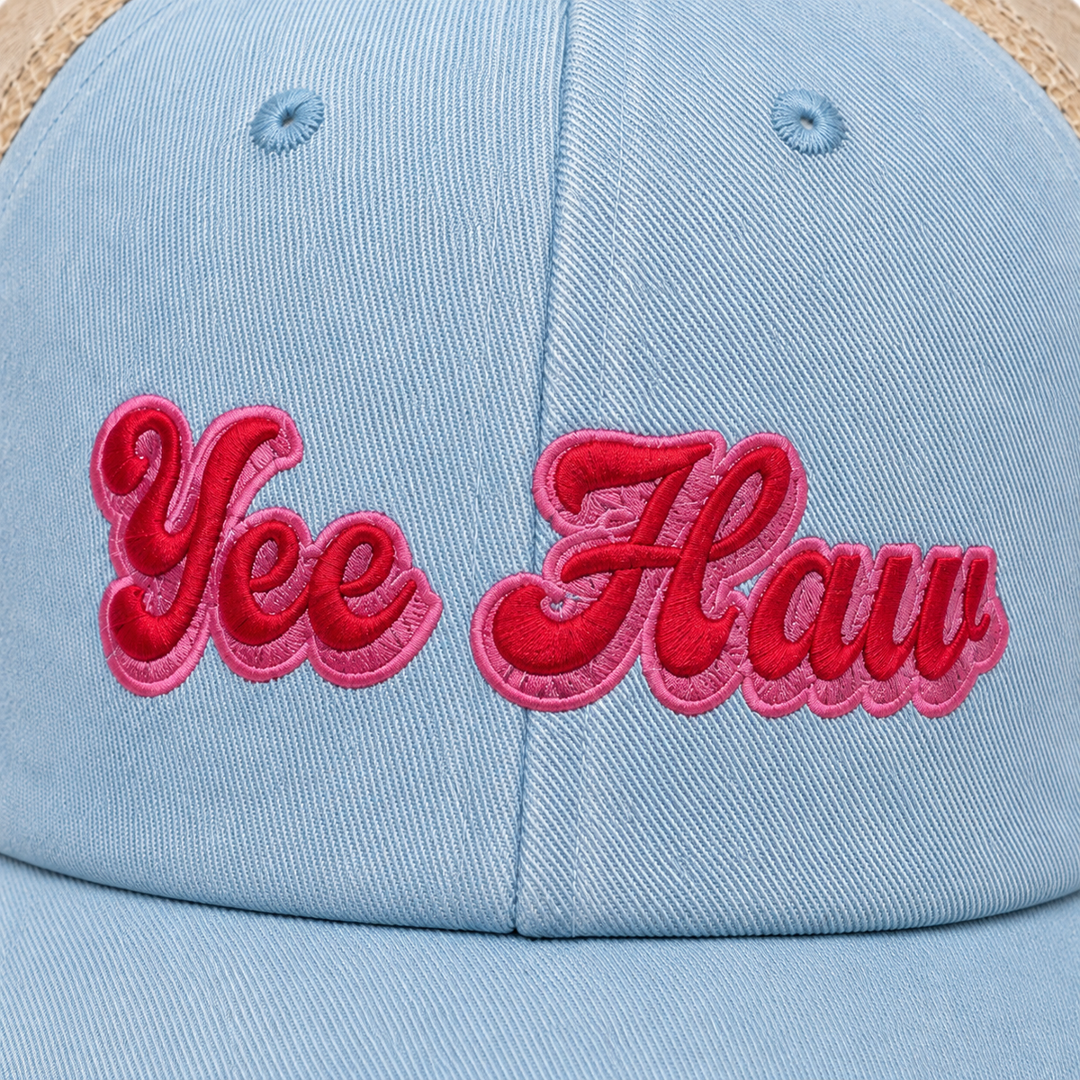 Close-up of Yee Haw trucker hat showing raised pink and red embroidered lettering on light blue denim