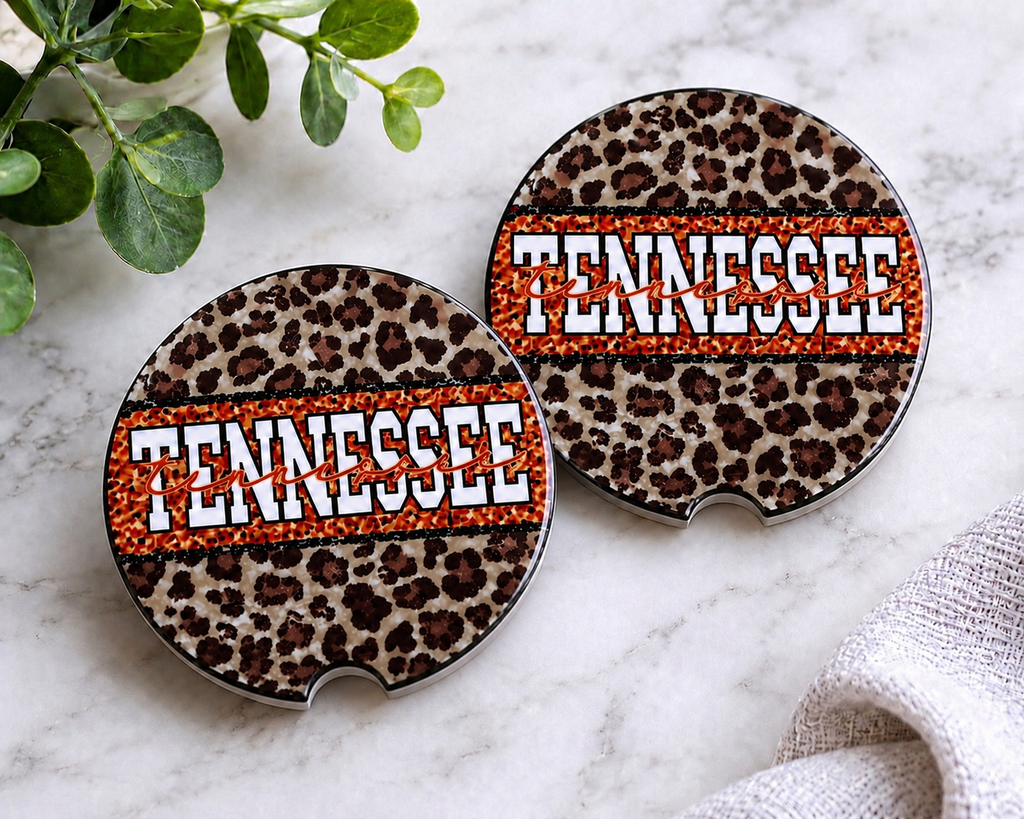Tennessee Leopard Car Coaster Set — set of 2 ceramic coasters with leopard print and bold orange "Tennessee" block lettering with script overlay, on marble surface
