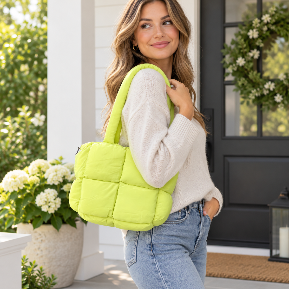 Woman in cream sweater and jeans carrying Lime Mini Puffer Tote Bag on shoulder showing bright lime green large-panel puffer quilted nylon and dual tubular puffer handles on white farmhouse porch with white hydrangeas and black front door
