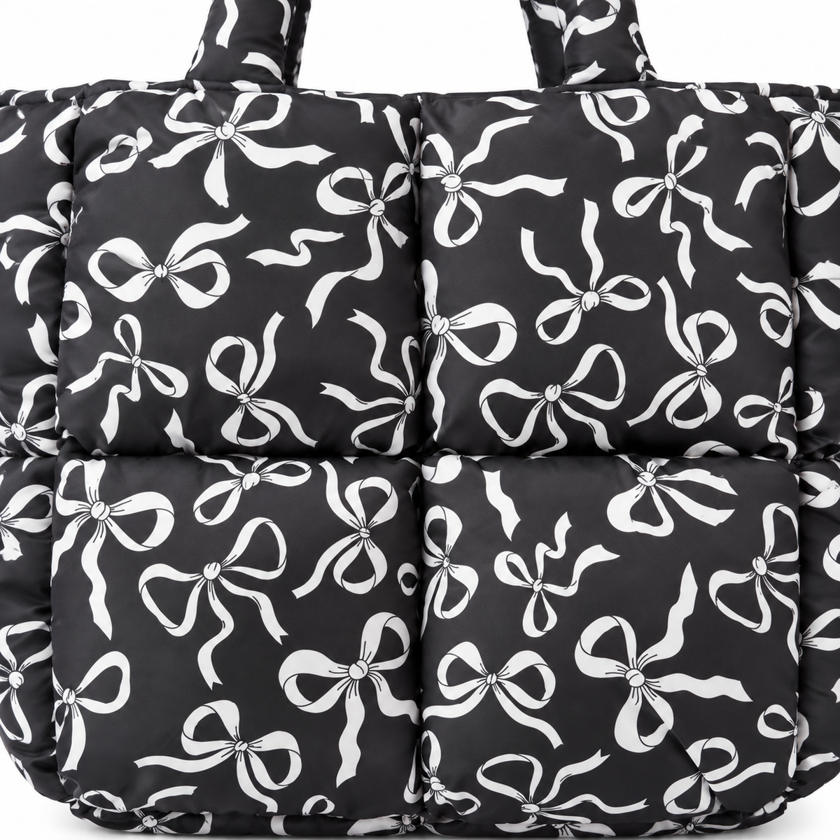 Close-up of Black Bow Print Puffer Tote showing all-over white bow print detail with silver center hardware on black puffer quilted panels
