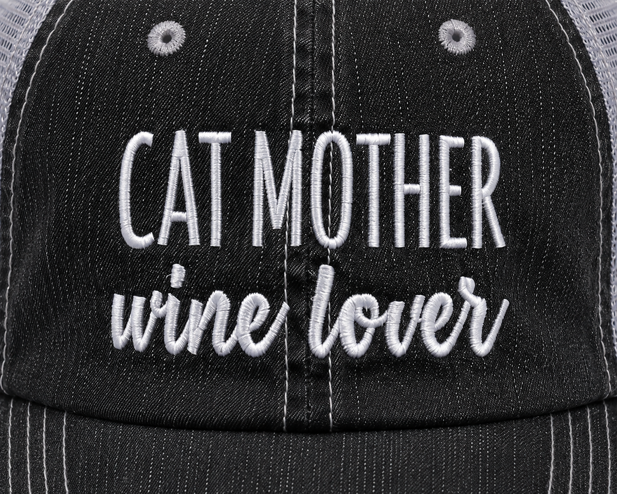 Close-up of white embroidered "Cat Mother Wine Lover" lettering on a distressed black trucker hat front panel.
