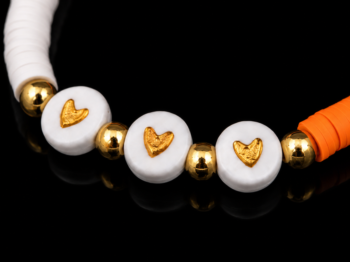 Close-up of three white disc beads with gold heart accents flanked by gold-tone spacer beads on orange and white bracelet
