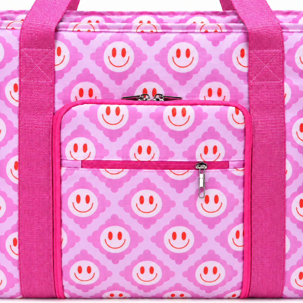 Close-up of Pink Smiley Flower Weekender Bag showing light pink all-over smiley face quatrefoil print with hot pink vertical trim straps, upper silver-zip slip pocket, and lower hot pink zippered front pocket with silver pull tab
