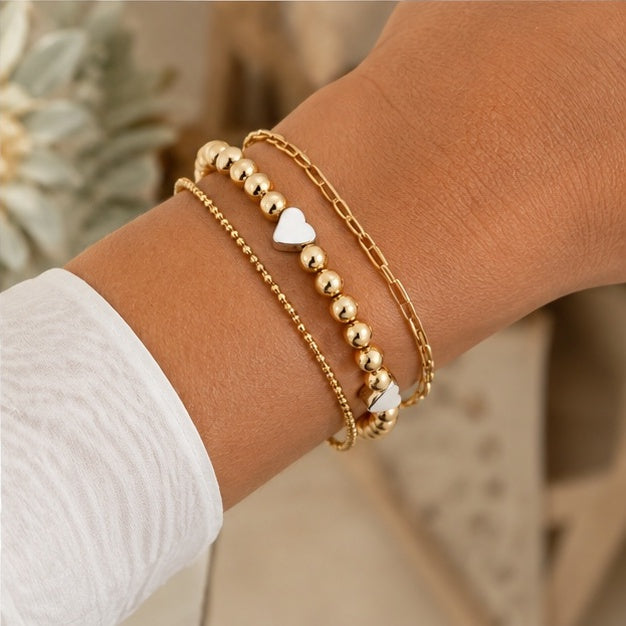 Gold and silver heart beaded bracelet stacked with two other gold bracelets on wrist

