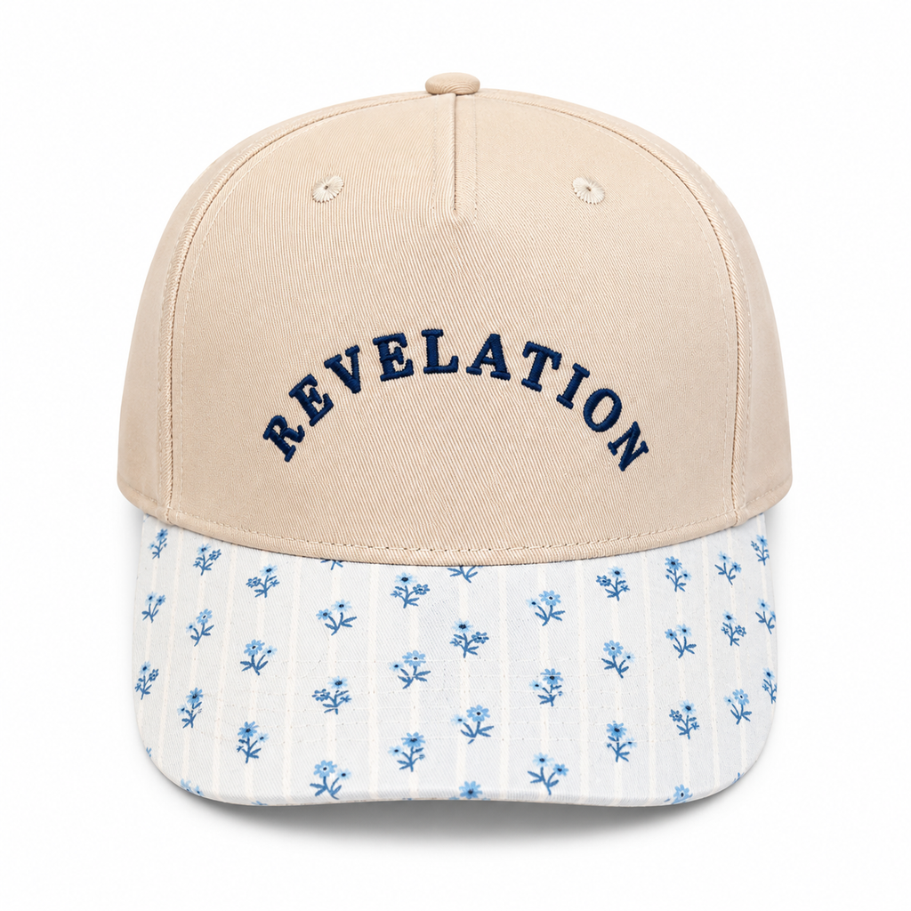 Revelation Baseball Cap in sand crown with navy embroidered lettering and blue floral-print brim, shown on a white background.
