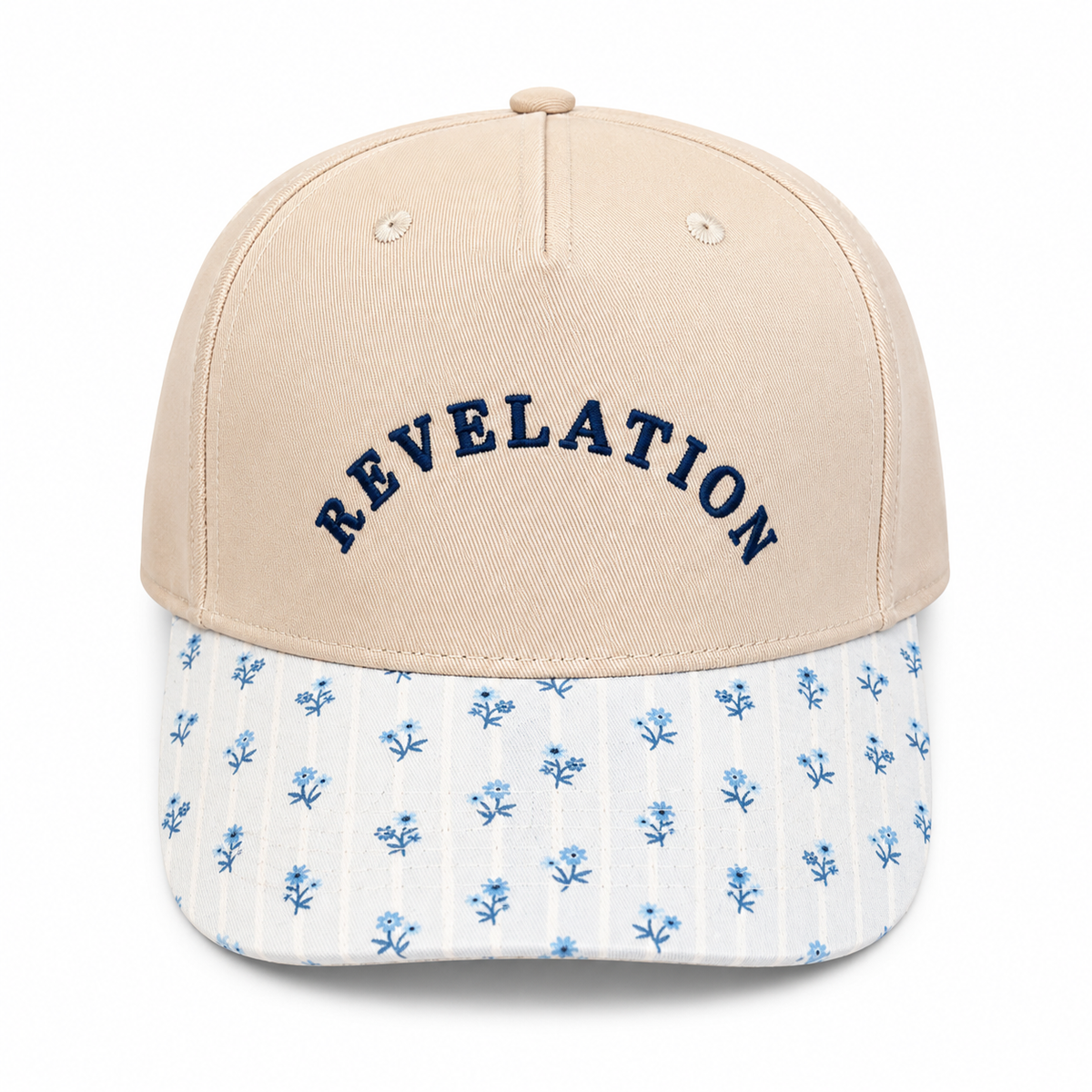 Revelation Baseball Cap in sand crown with navy embroidered lettering and blue floral-print brim, shown on a white background.
