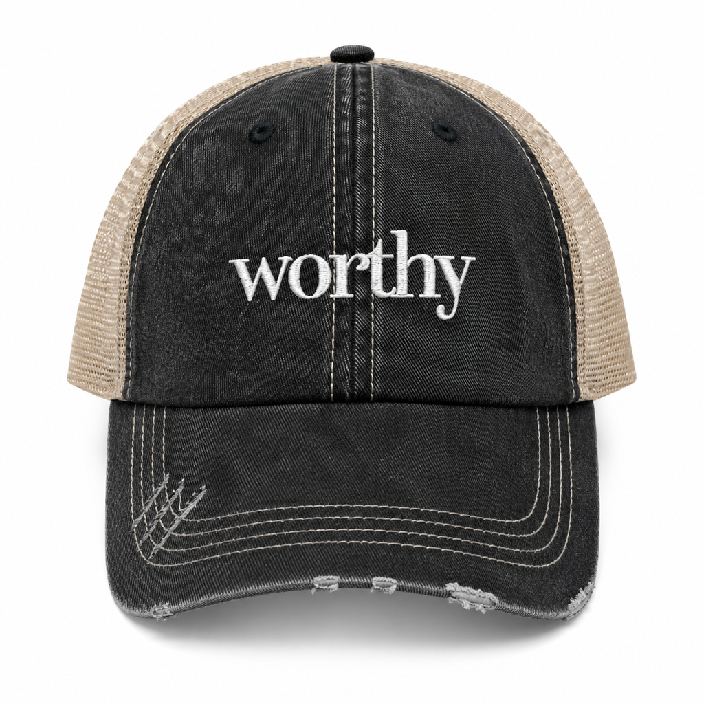 A distressed trucker cap with a washed black front panel and brim, beige mesh back panels, and white embroidered text reading 'worthy' on the front, shown against a plain white background.