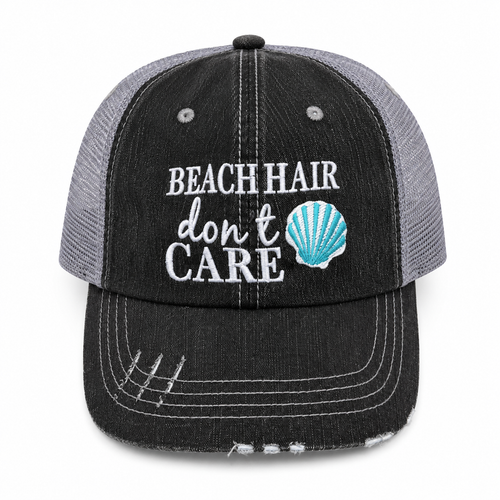 Beach Hair Don't Care trucker hat in distressed black denim front with white embroidery and teal seashell detail, shown on a white background.
