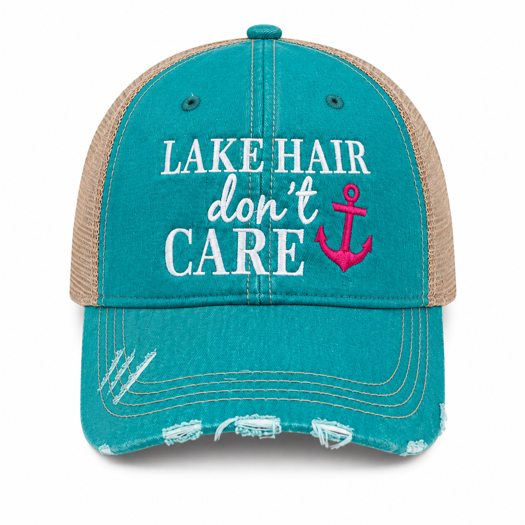 A distressed trucker hat in teal and tan mesh, featuring the text 'LAKE HAIR don't CARE' in white and pink embroidered lettering with a pink anchor graphic on the front.